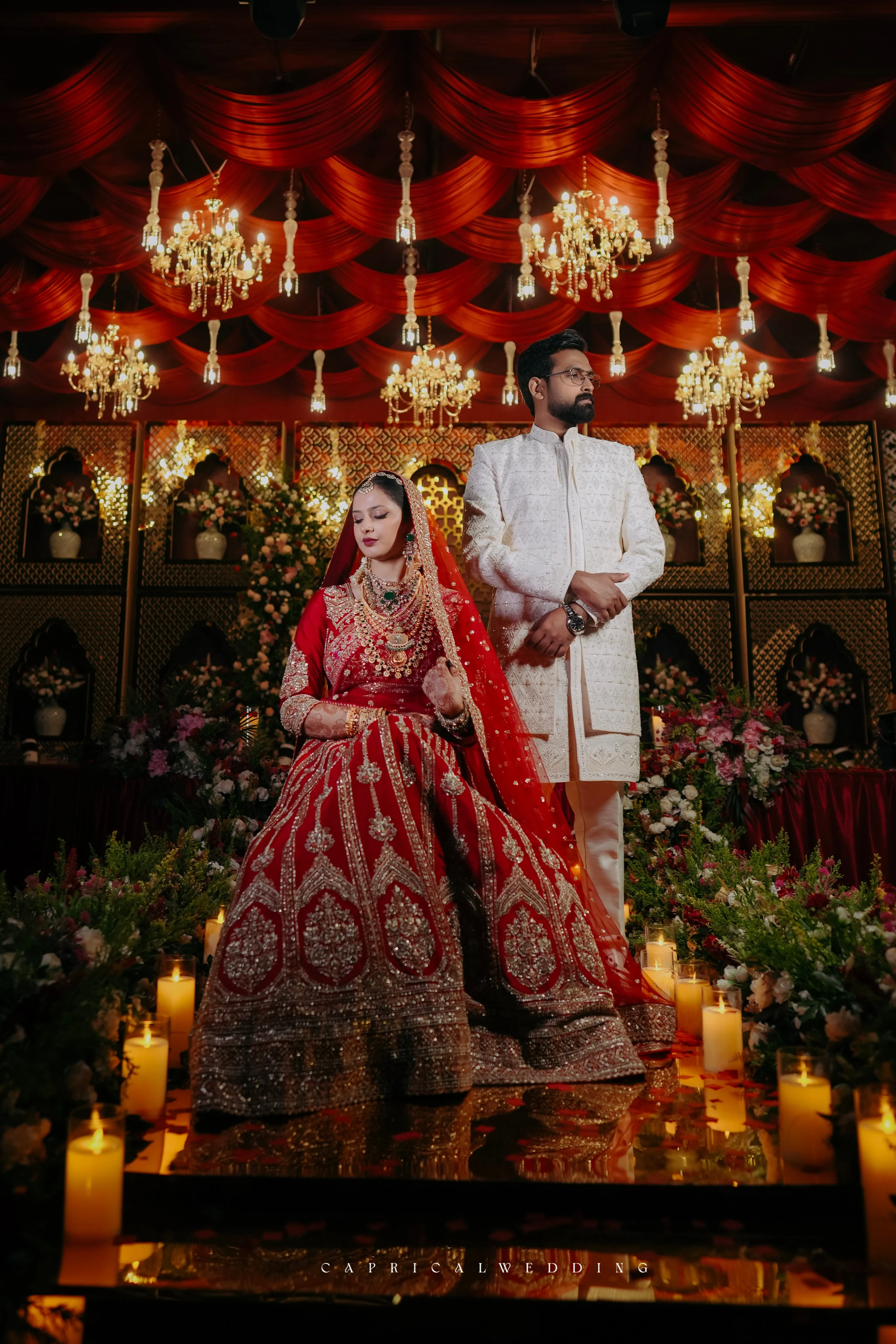 A couple in red and ivory beneath ornate wedding chandeliers